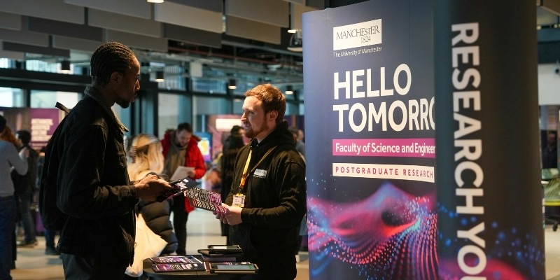 People talking at a postgraduate research event beside a Faculty of Science and Engineering display.