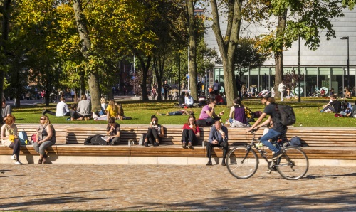 people walking and cycling through a campus park on sunny day surrounded by greenery