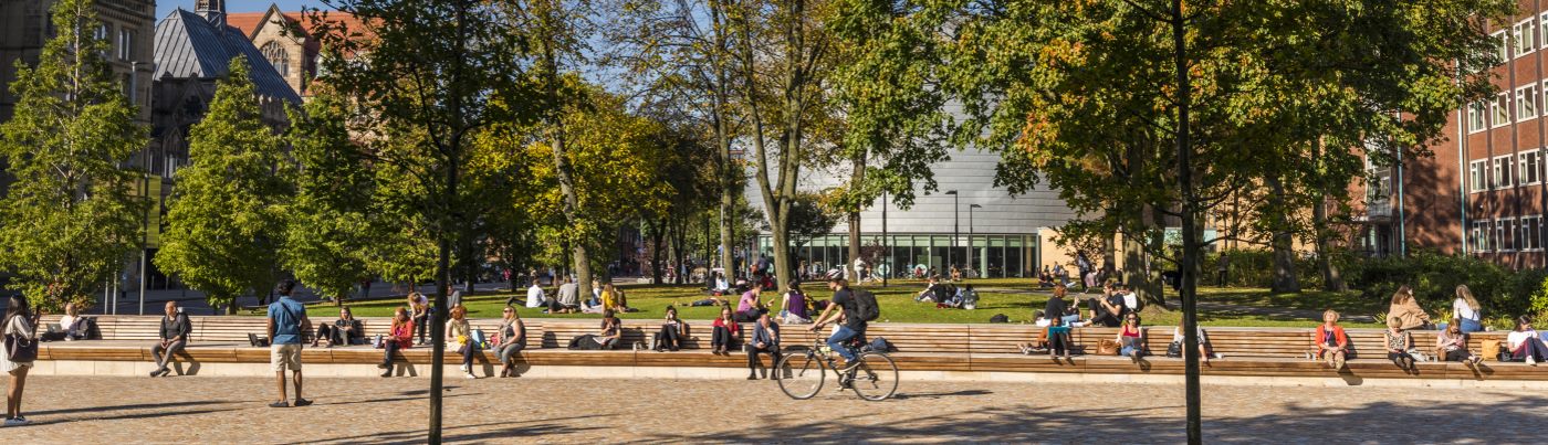 People sat and cycling through a campus park on sunny day surrounded by greenery