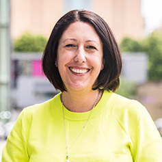 Profile of a lady wearing a bright yellow top and smiling