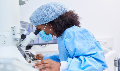 Female scientist dressed in full personal protective equipment, looking into a microscope