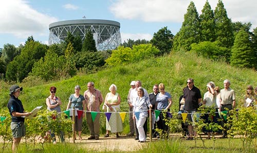 Group of people in a field on a sunny day with the Lovell Telescope in the background