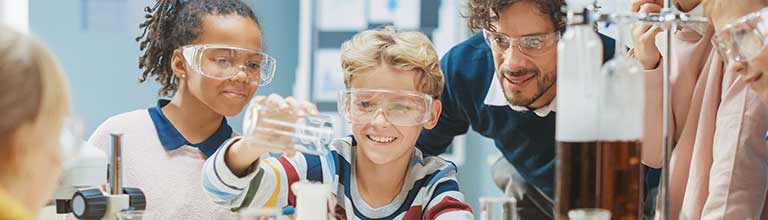 Three children and a man wearing protective glasses and pouring liquid into a beaker