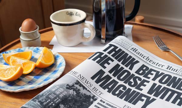 A table with a newspaper titled: Think Beyond the Noise with Magnify, coffee and orange slices.