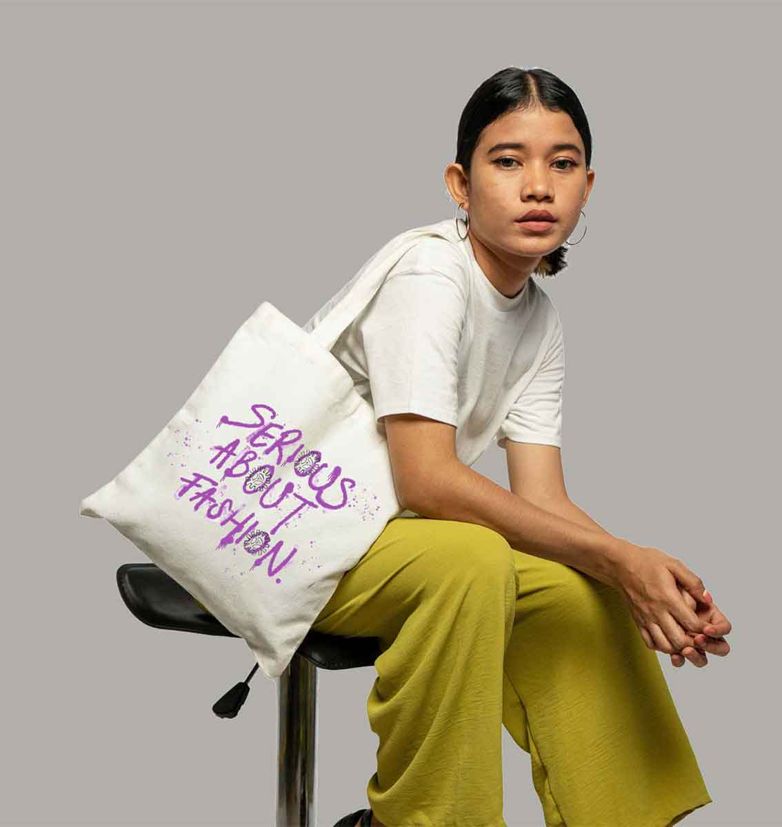 Female sat on a chair with a tote bag on her shoulder that reads Serious About Fashion