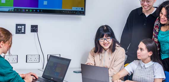 Group of people looking at a laptop and stood next to a screen showing the map of a project