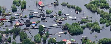 Aerial view of houses and trees set within a large body of water that connect with a jetty 