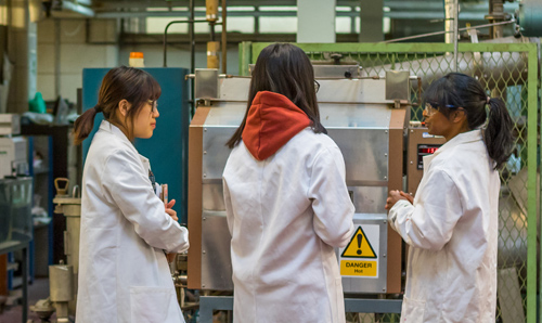 3 females wearing white labcoats in discussion