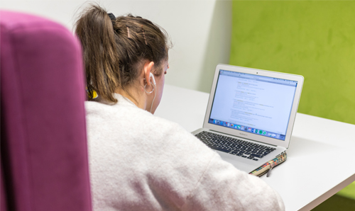 A student, wearing earphones, sat at desk with Macbook