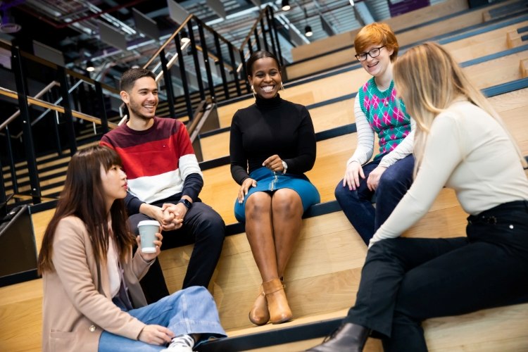 Five postgraduate researchers chatting in the foyer of the University's Nancy Rothwell Building.