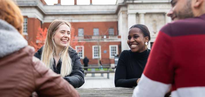 Four researchers sat smiling at a wooden table in front of a historic building