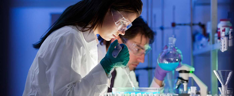 A female scientists uses a pipette to drop liquid into a series of test tubes.