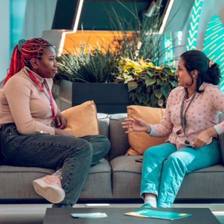 Manchester researchers, Chithra and Leona, chatting on a sofa in a foyer at the Henry Royce Institute.