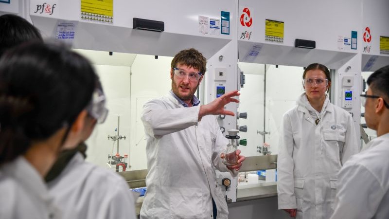 Person in lab coat explaining an experiment to a group in a University of Manchester lab.