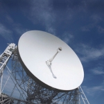 A photo of the Jodrell Bank Observatory against a blue sky, taken from ground level.