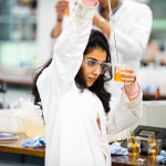 A student holds a gas-inlet tube above a beaker while conducting a Chemistry experiment in the laboratories at The University of Manchester.