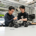 Two students work collaboratively on a small, wheeled robotic vehicle in a workshop at The University of Manchester.