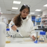 A researcher in a white lab coat uses a pipette to dispense liquid onto a petri dish in a lab in The University of Manchester's Stopford Building.