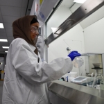A University of Manchester student wearing safety goggles and a white lab coat works in a fume hood in a lab.