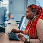 A researcher at The University of Manchester with red braided hair working on a computer in an office environment.