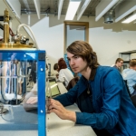 A student wearing a blue jacket working with scientific apparatus in at a University of Manchester Physics lab.