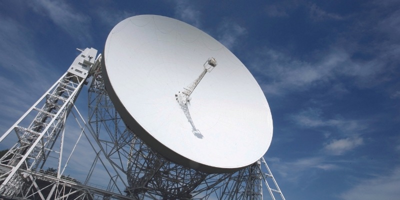 A photo of the Jodrell Bank Observatory against a blue sky, taken from ground level.
