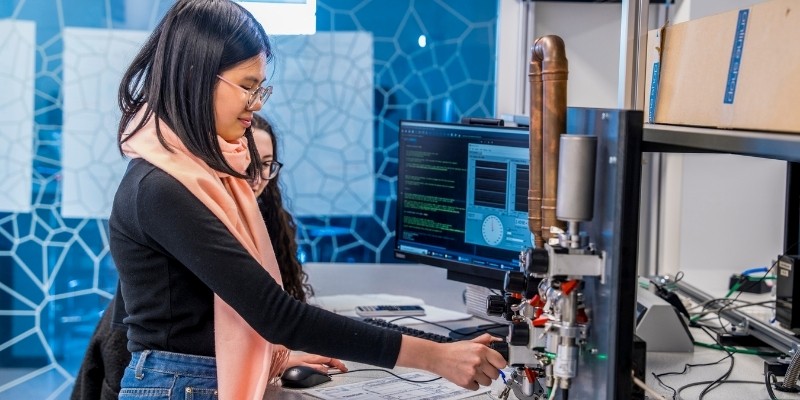 Smiling student adjusting controls on a lab machine in the Schuster Building.