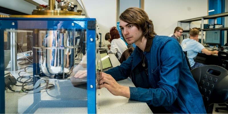 A student wearing a blue jacket working with scientific apparatus in a University of Manchester lab.