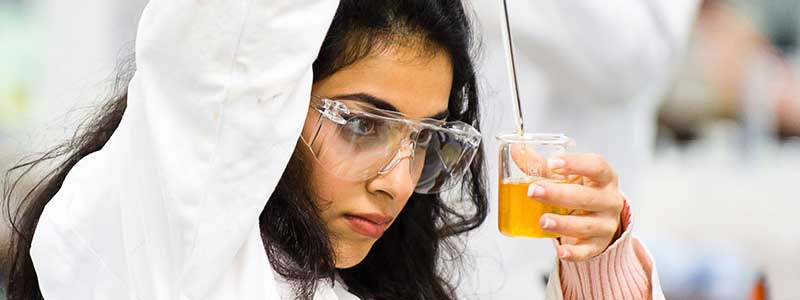 Researcher wearing safety goggles examining a liquid sample in a laboratory.