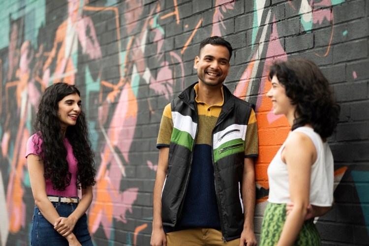 Three University of Manchester’s students chatting outside a wall art instillation in Manchester.