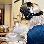 Female in a lab wearing a protective face shield and pouring chemicals
